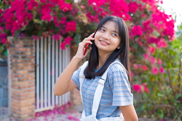 Young asian girl talking on the phone outdoor beautiful flower background
