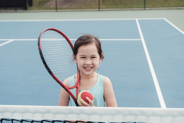 Young Asian girl tennis player on outdoor blue court