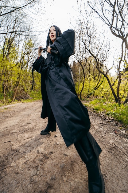 Foto giovane ragazza asiatica in kimono nero tradizionale con la spada sullo sfondo della natura