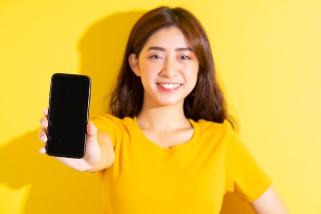 Smartphone di uisng giovane ragazza asiatica su colore giallo