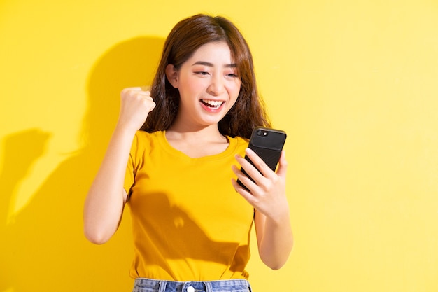 Young asian girl uisng smartphone on yellow