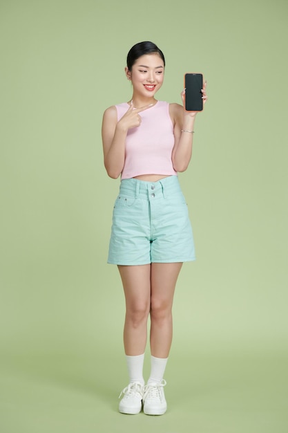 Молодая азиатская девушка с помощью телефона на зеленом фоне