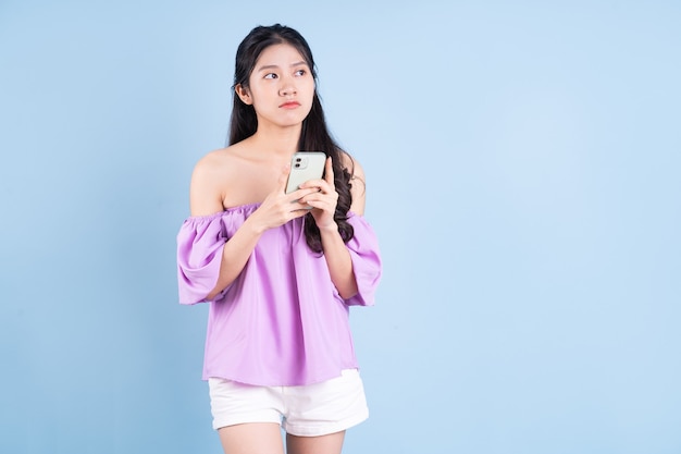 Young Asian girl using smartphone on blue background