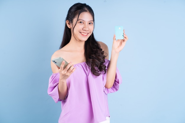Молодая азиатская девушка с помощью смартфона на синем фоне
