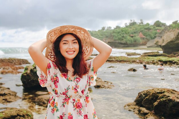 Foto una giovane ragazza asiatica che indossa un cappello da spiaggia si sta rilassando sulla spiaggia del cielo blu a gunungkidul indonesia