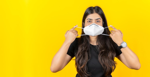 Young Asian girl wearing a medical face mask in casual clothing isolated on yellow background