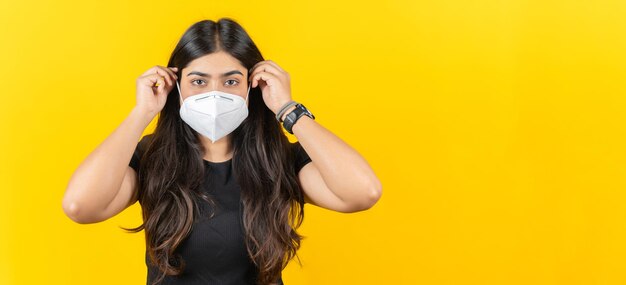 Young Asian girl wearing a medical face mask in casual clothing isolated on yellow background