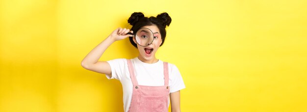 Young asian girl with bright makeup look through magnifying glass smiling excited seeing interesting