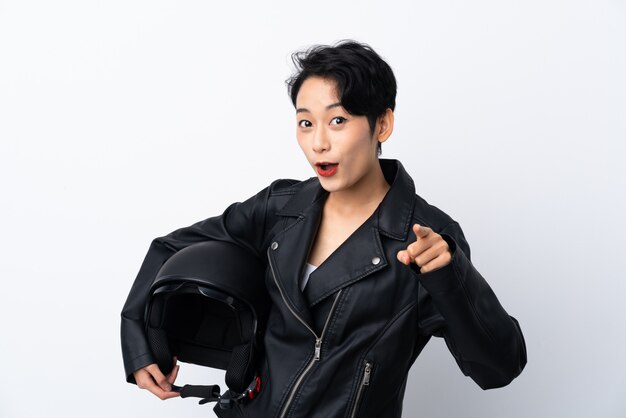 Young Asian girl with a motorcycle helmet over isolated white wall surprised and pointing front