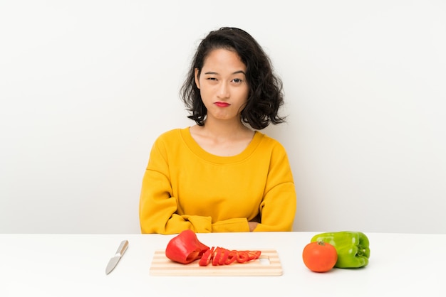 Giovane ragazza asiatica con le verdure in una tabella triste