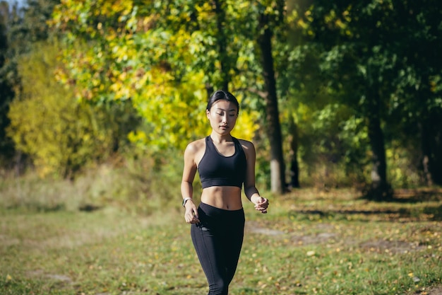 写真 森や都市公園でジョギングする若いアジアの幸せな女性ランナー。朝のジョギング。アクティブで健康的なライフスタイル。魅力的なフィットネス女性。屋外でのスポーツトレーニング。新鮮な空気の中でのアスリートトレーニングランエクササイズ