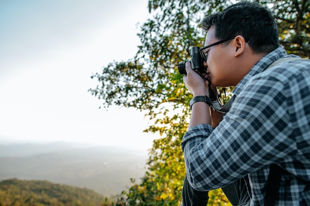 Young Asian hiker man and backpack use camera to take pictures in forest copy space