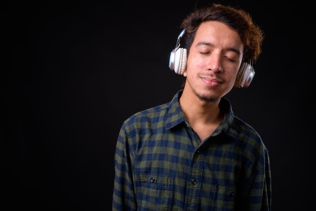 young Asian hipster man with curly hair and acne against black space