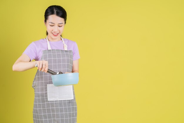젊은 아시아 주부 가 노란색 배경 에 포즈 를 취 하고 있다
