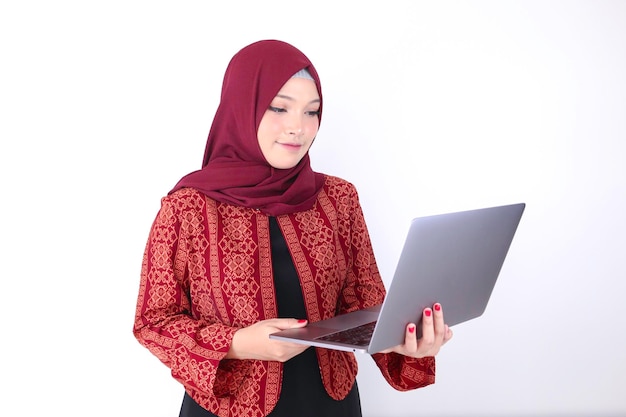 Young Asian Islam woman is standing and smiling face with hand holding laptop