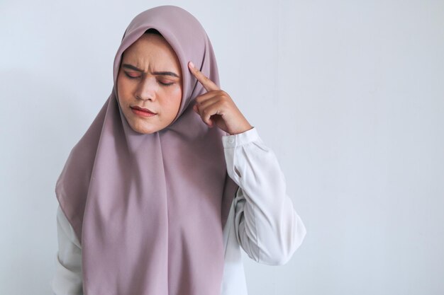 Young Asian Islam woman wearing headscarf is putting a finger on the cheek with thinking and looking up to copy space Smiling Indonesian woman on gray background