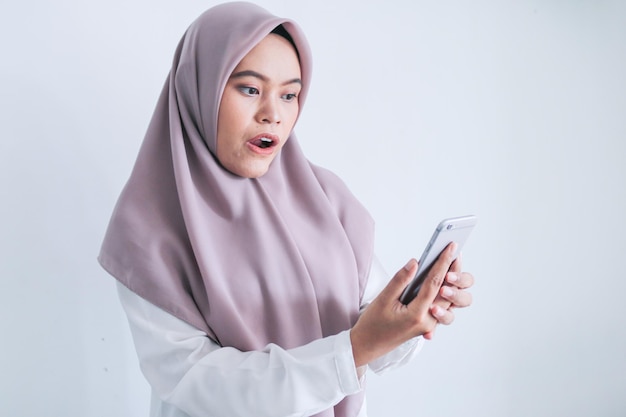 Young Asian Islam woman wearing headscarf is shocked and wow in the smartphone Indonesian woman on gray background