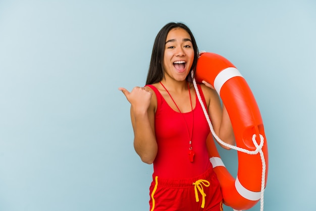 Young asian lifeguard woman points with thumb finger away, laughing and carefree.