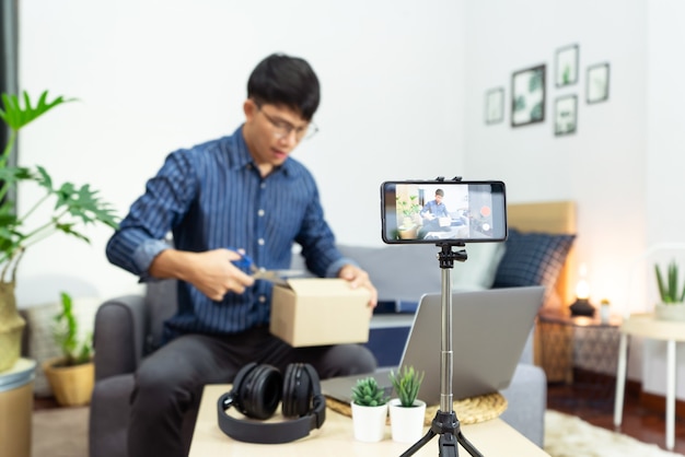 Young asian male blogger recording vlog video on camera review of product at home office, Focus on tripod mounted camera screen broadcast live stream video to a social network.