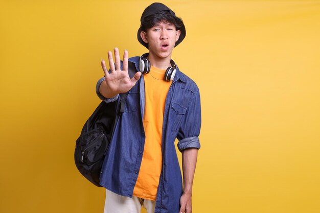 Young Asian male in casual style showing stop sign gesture standing against yellow background