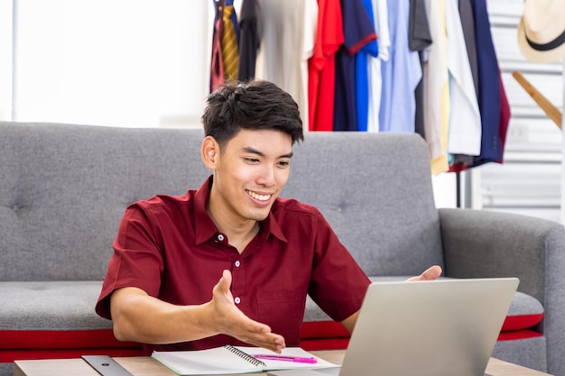 Young Asian male online merchant freelance blogger is working business from home with laptop with thump up looking at camera Social media teleconference and online shopping concept