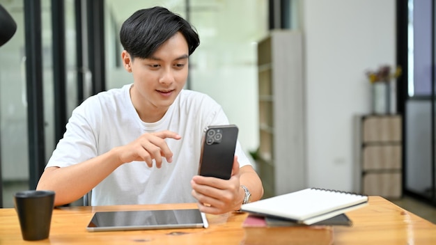 Молодой азиатский мужчина с помощью смартфона прокручивает сообщения в социальных сетях своим друзьям
