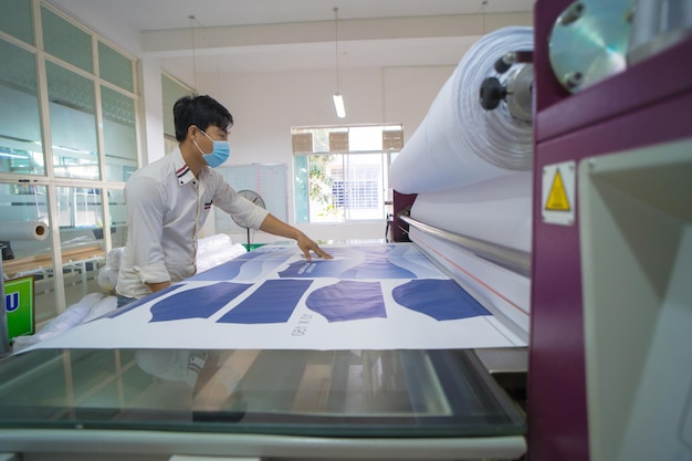 Photo young asian male worker technician wearing medical mask make object on sublimation heat press