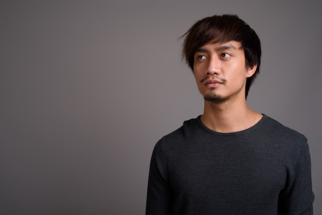 Young Asian man against gray wall