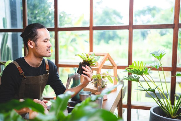 写真 若いアジア人男性は、自宅の小さな緑豊かな庭で植物を育てること、家の中で緑の自然と趣味のライフスタイル、植物園の農業栽培にポットの花の木に満足しています
