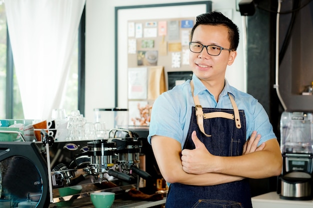 Young asian man barista standing at coffee cafe counter background