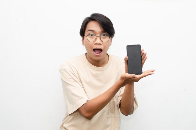 young asian man in beige tshirt holding and showing phone screen with happy euphoric shocked face