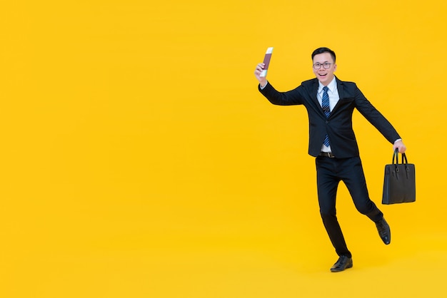 Young Asian man in business suit with bag showing passport and boarding pass about to go for travel