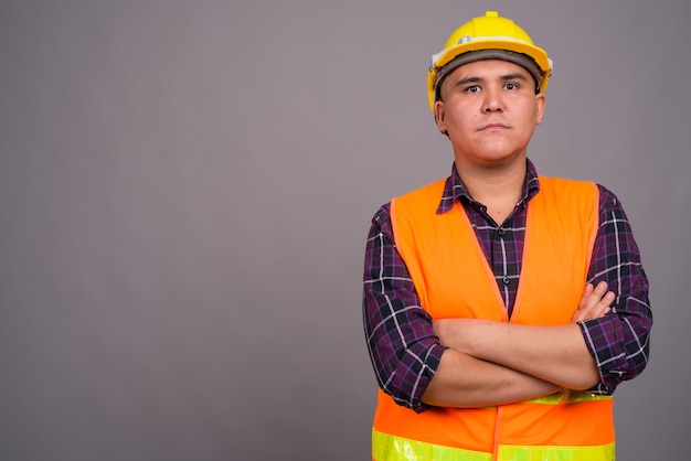 young Asian man construction worker against gray wall