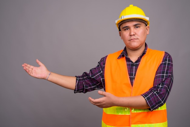 young Asian man construction worker against gray wall