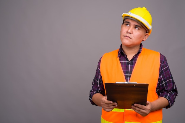 young Asian man construction worker against gray wall