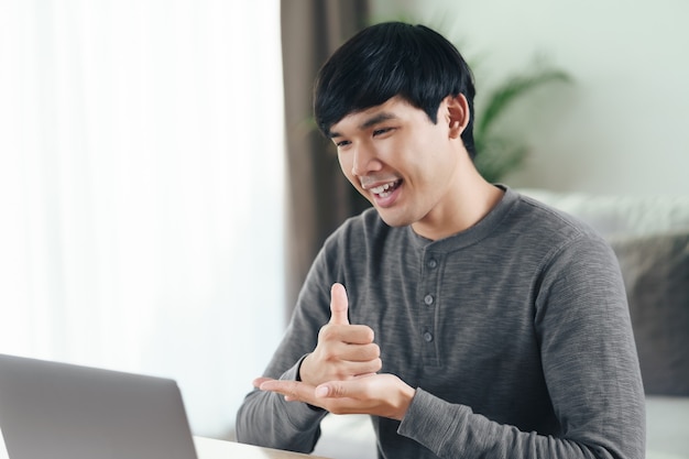 Young Asian man deaf disabled using laptop computer for online video conference call learning and communicating in sign language.