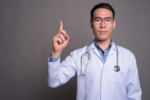 Young Asian man doctor against gray wall