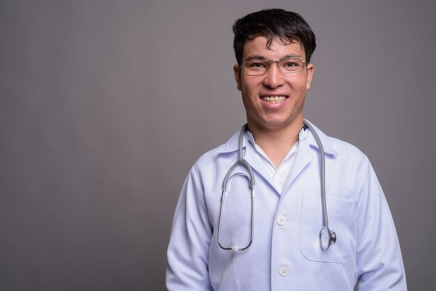 Young Asian man doctor against gray wall