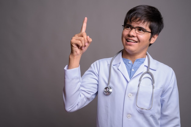 Young Asian man doctor against gray wall