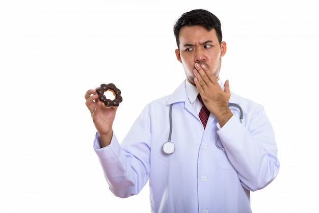 Молодой азиатский мужчина доктор держит пончик во время просмотра