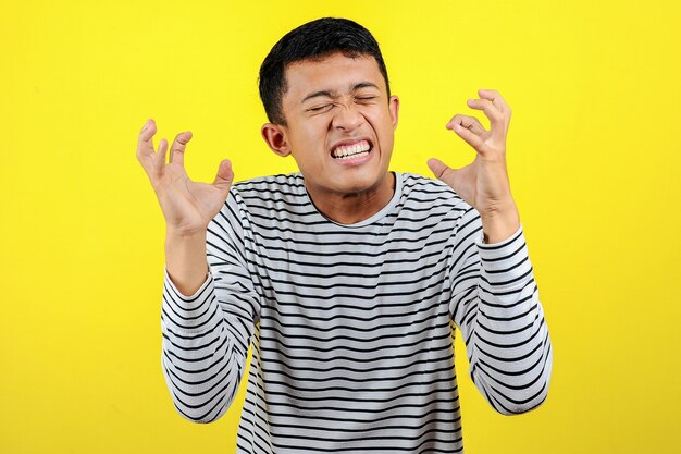 Young Asian man doing angry gesture, annoyed, and emotional, isolated on yellow background