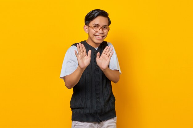 Young Asian man doing stop gesture with hands palms isolated over yellow background