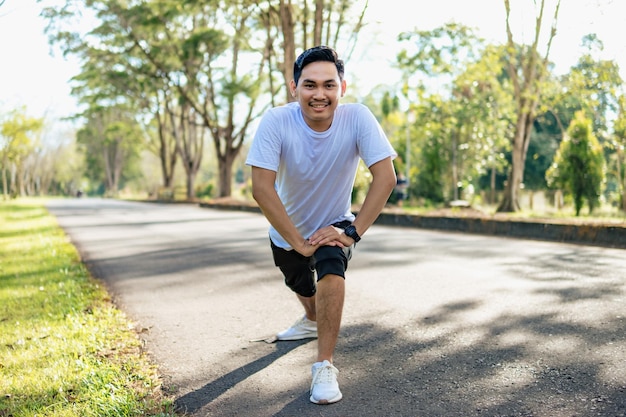Молодой азиатский мужчина делает упражнения на растяжку, готовясь к бегу на природе Здоровый образ жизни