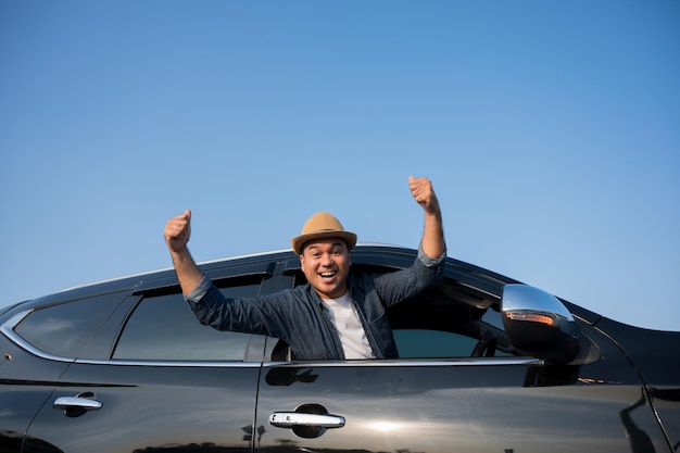 若いアジア人男性が晴れた日に車を運転します。美しい青い空。彼は車で旅行するために運転している。