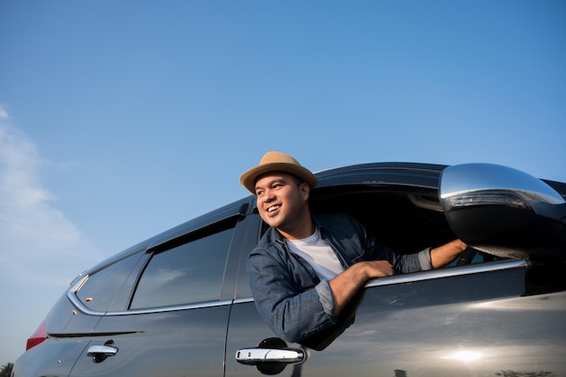 A young Asian man drives a car on a clear day. With beautiful blue sky. He driving to travel by car.