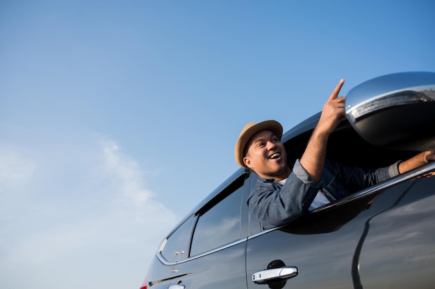 若いアジア人男性が晴れた日に車を運転します。美しい青い空。彼は車で旅行するために運転している。