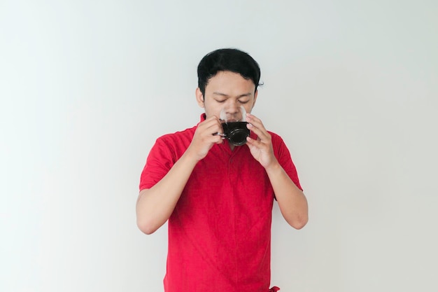 Young Asian man enjoy drinking a cup of coffee standing over isolated white background