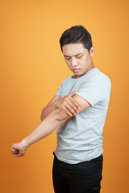 Young asian man feel hurting his arm standing isolated on\
orange background