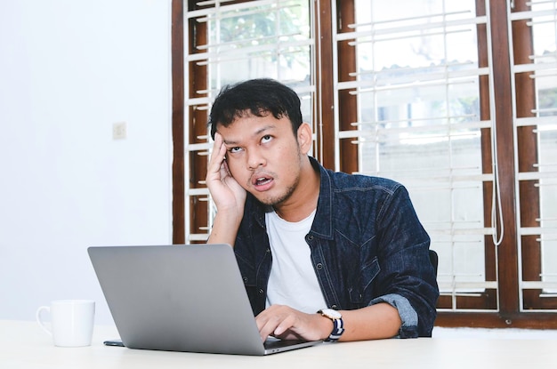 Young Asian man feeling stress and confuse when work laptop on table