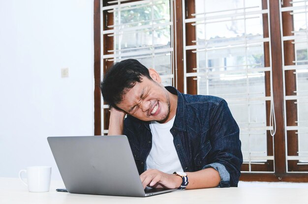 Young Asian man feeling stress and confuse when work laptop on table